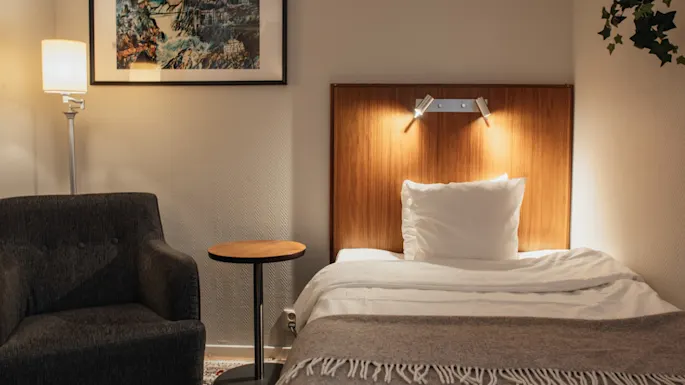 Home Hotel Kung Oscar – Compact Cabin – Et koselig hotellrom med en enkeltseng, en lenestol og et sidebord, opplyst av myk belysning.
