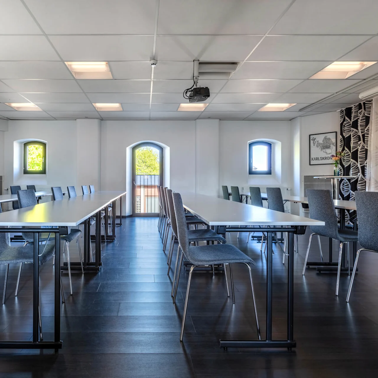 A conference room with rows of tables and chairs, centered towards a projector screen, in a clean and modern setting.