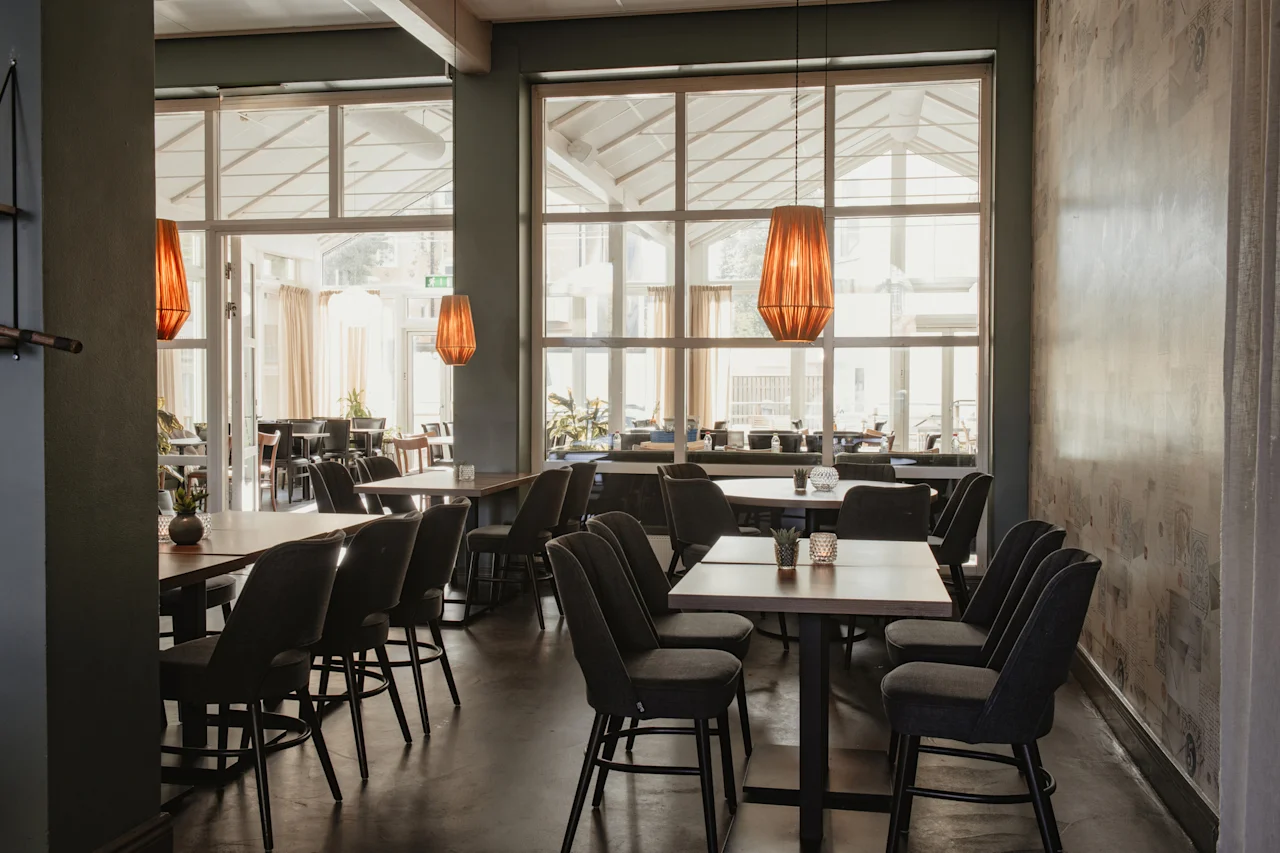 Home Hotel Post. En ljus och inbjudande restaurangmatsal med bord, stolar och stora fönster som vetter mot en annan matplats.