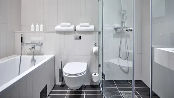 Bathtub, toilet, and shower are arranged neatly in a modern bathroom with white tiles and dark floor tiles. Towels and soap dispensers are on a shelf above the bathtub.