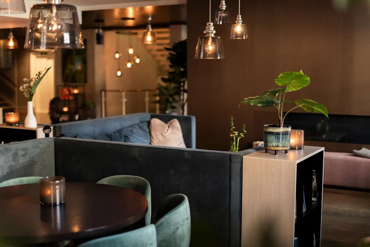 Et varmt og indbydende loungeområde med komfortable siddepladser, blød belysning og dekorative planter, der skaber en hyggelig atmosfære.