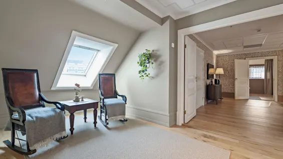 A cozy attic room with two rocking chairs and a small table under a skylight, inviting relaxation and quiet moments.