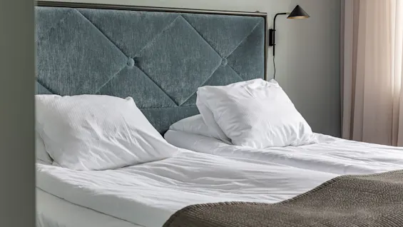 A neatly made bed with white linens; plush headboard, warm lighting, serene décor.