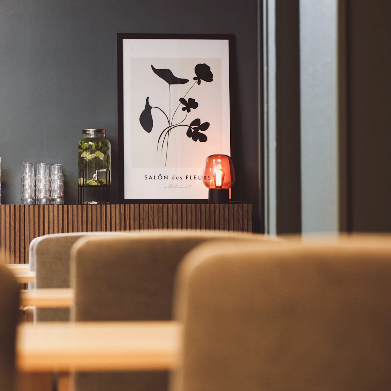 A framed botanical print hangs above a sideboard with a jar of greens, glasses, and a red lamp in a cozy dining area. Text reads: "SALON des FLEURS."