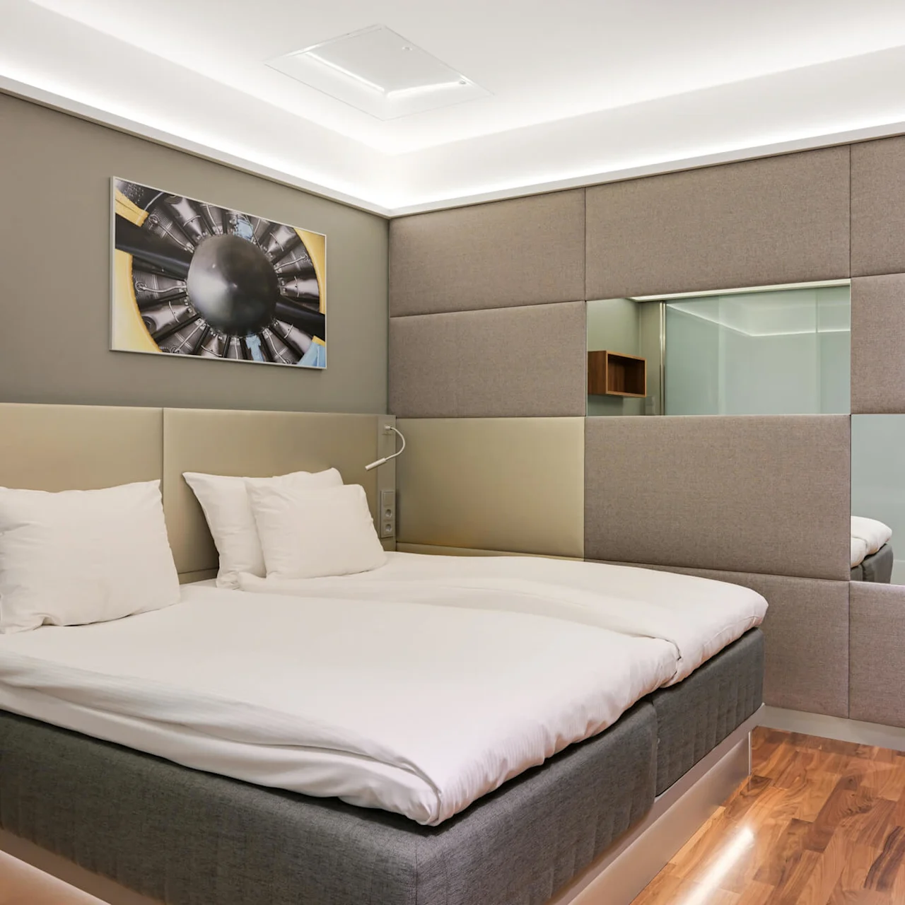 Ett modernt hotellrum med en snyggt bäddad dubbelsäng med vita sängkläder. Väggkonst, eleganta trämöbler och mjuk belysning skapar en minimalisk, mysig atmosfär.