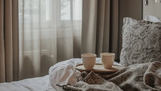 Two cups on a tray on a bed, with soft light filtering through curtains, creating a cozy and relaxing atmosphere.