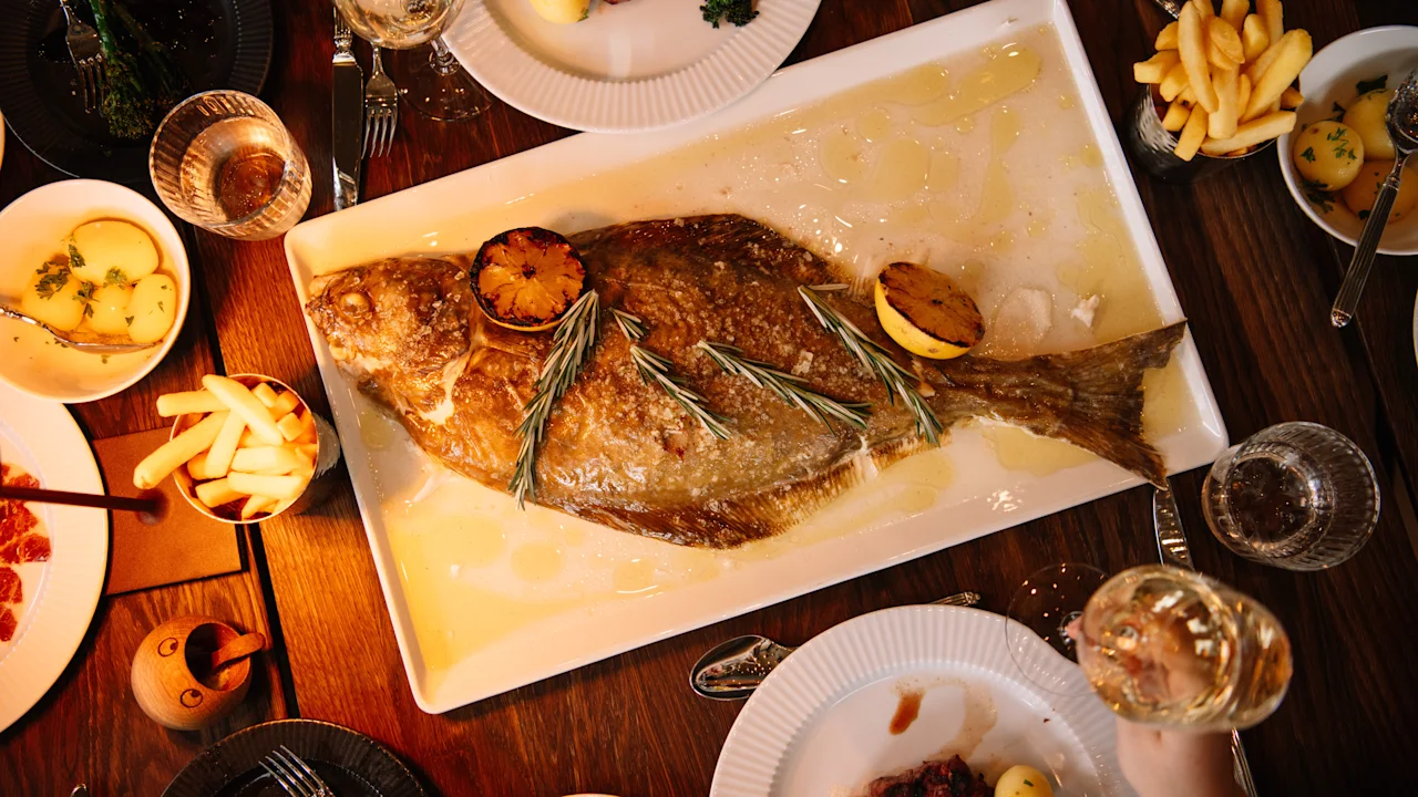 En stor ovnbagt fisk serveres med tilbehør på en restaurant på KG Hotel.