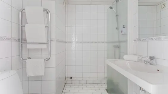 A bright, clean bathroom with white tiles, featuring a shower, sink, and fresh towels on a heated rack.