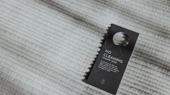 På "Ingen städning"-skylten står det på ett texturerat, ljusfärgat tygunderlag: "NO CLEANING THANK YOU. In efforts to protect the environment, we are using fewer chemicals and generating less waste by cleaning every other day."