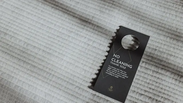 På "Ingen städning"-skylten står det på ett texturerat, ljusfärgat tygunderlag: "NO CLEANING THANK YOU. In efforts to protect the environment, we are using fewer chemicals and generating less waste by cleaning every other day."