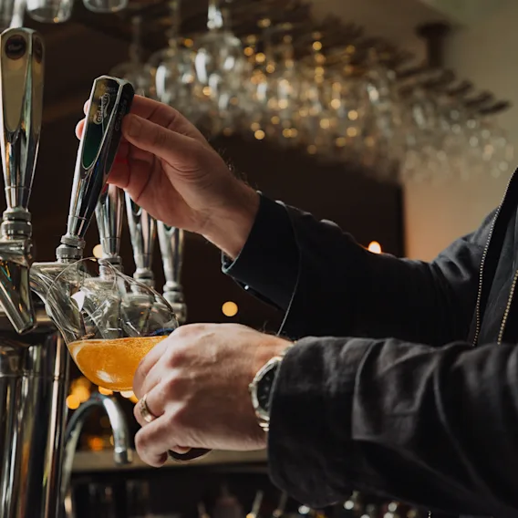 En bartender som häller upp en skummande fatöl från en kran i ett glas på en mysig bar.