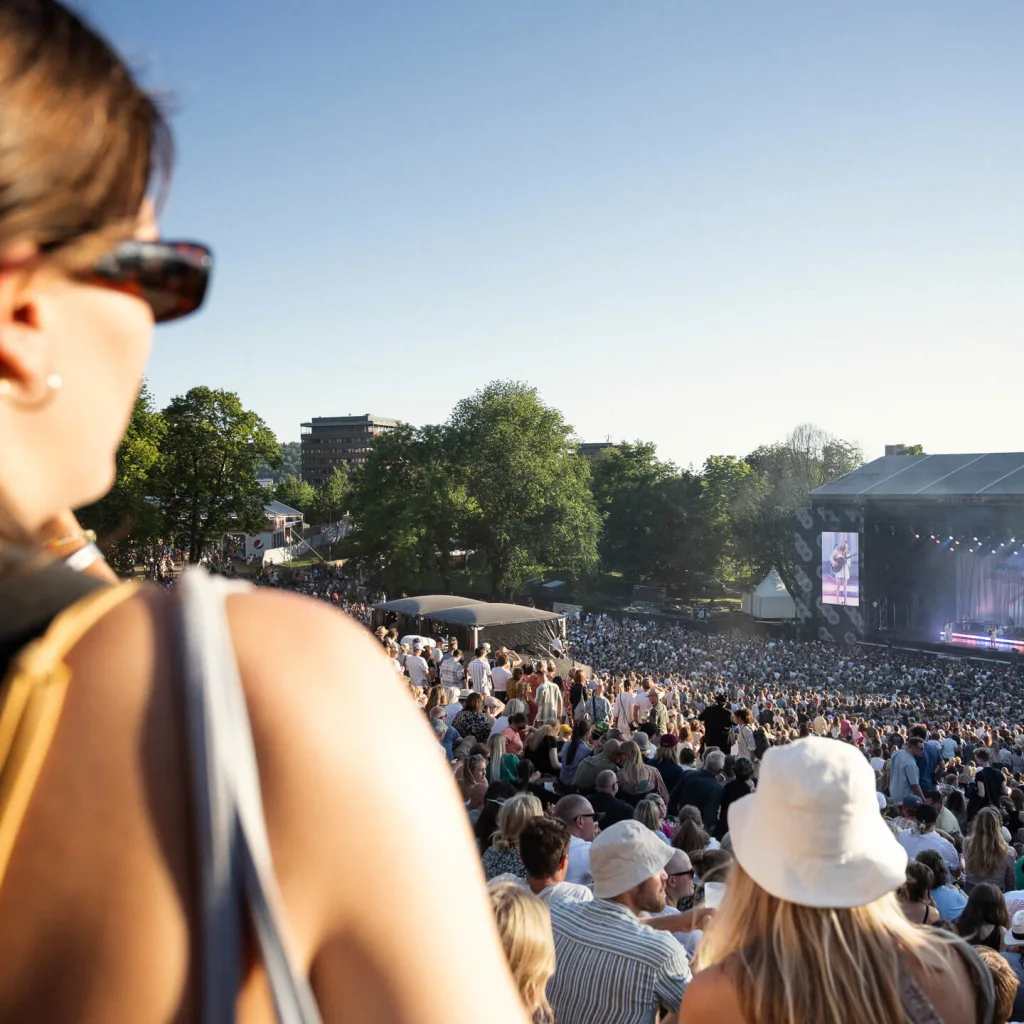 Nainen katselee väkijoukkoa ulkoilmakonsertissa, yleisö on keskittynyt kaukaiseen lavalle.