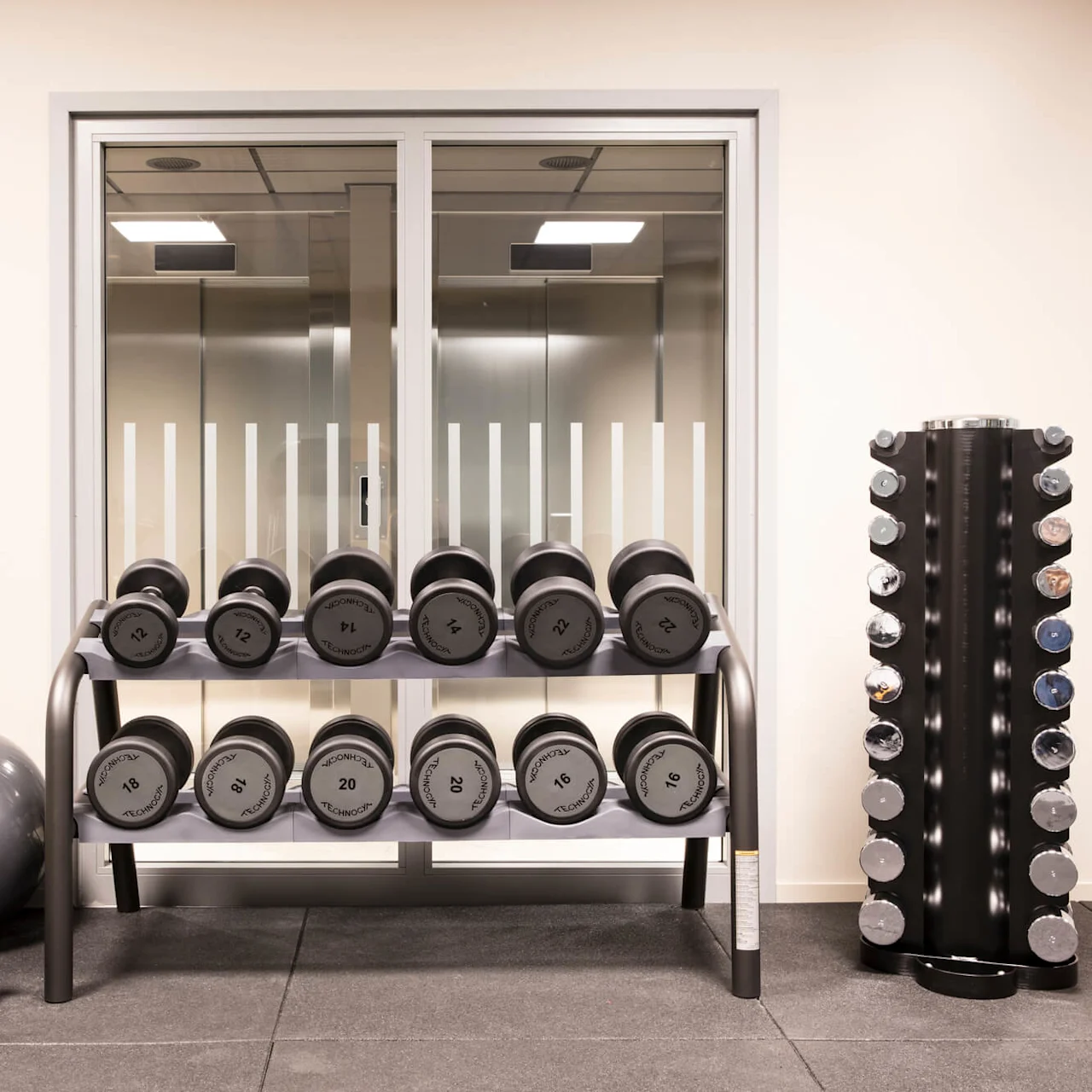Dumbbells arranged on a rack, exercise balls, and kettlebells in a tidy gym setting.