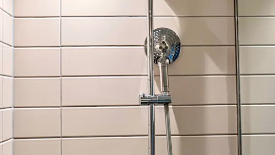 A modern shower with a rain shower head and a handheld shower, featuring a wall-mounted dispenser labeled HAIR & BODY.