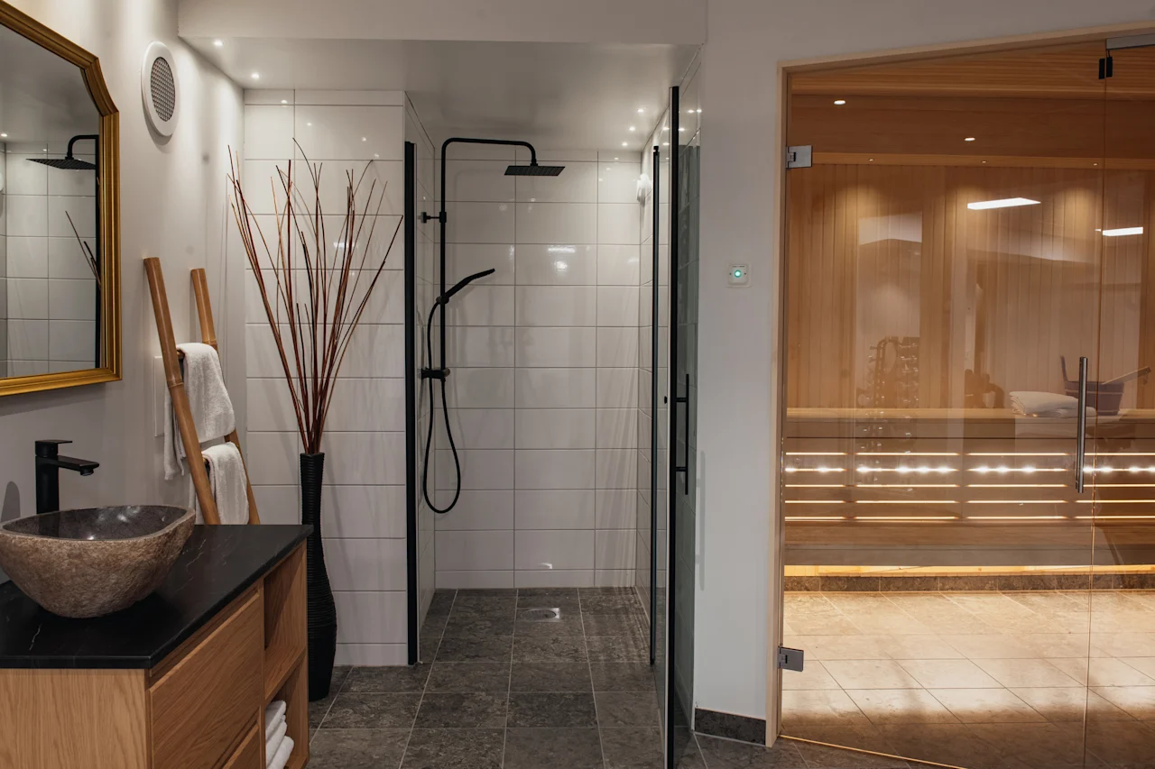 Ett modernt badrum med en walk-in-dusch, ett handfat med en unik diskho och en träbastu för avkoppling.