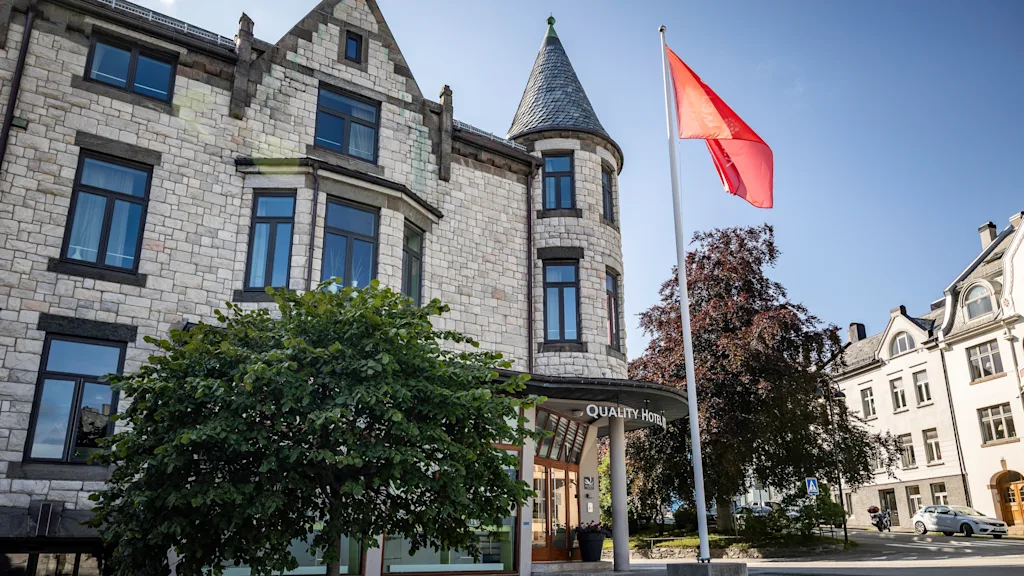 En steinbygning med et tårn og et rødt flagg som vaier. Inngangen har et skilt hvor det står "Hotell".