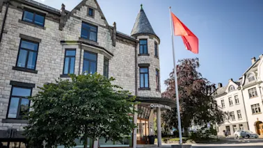 En steinbygning med et tårn og et rødt flagg som vaier. Inngangen har et skilt hvor det står "Hotell".