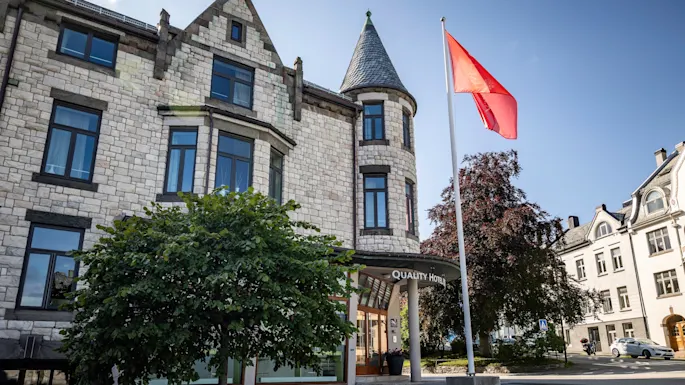 A stone building with a turret and a red flag flying. The entrance has a sign that reads "Hotel".