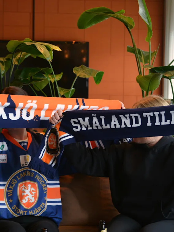 Tva supportrar som haller upp halsdukar i en sofa med texten Smaland tillhor oss