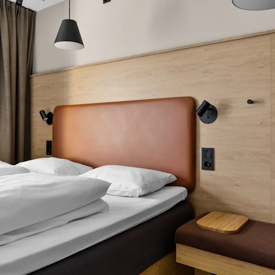 A cozy hotel room with a comfortable bed, warm lighting, and modern wooden accents.