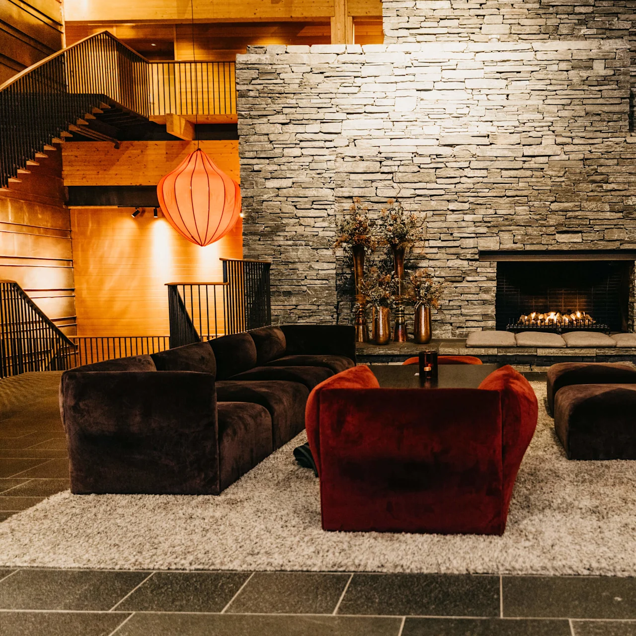 Plush sofas surround a lit fireplace in a cozy, well-lit room with stone walls and wooden accents.