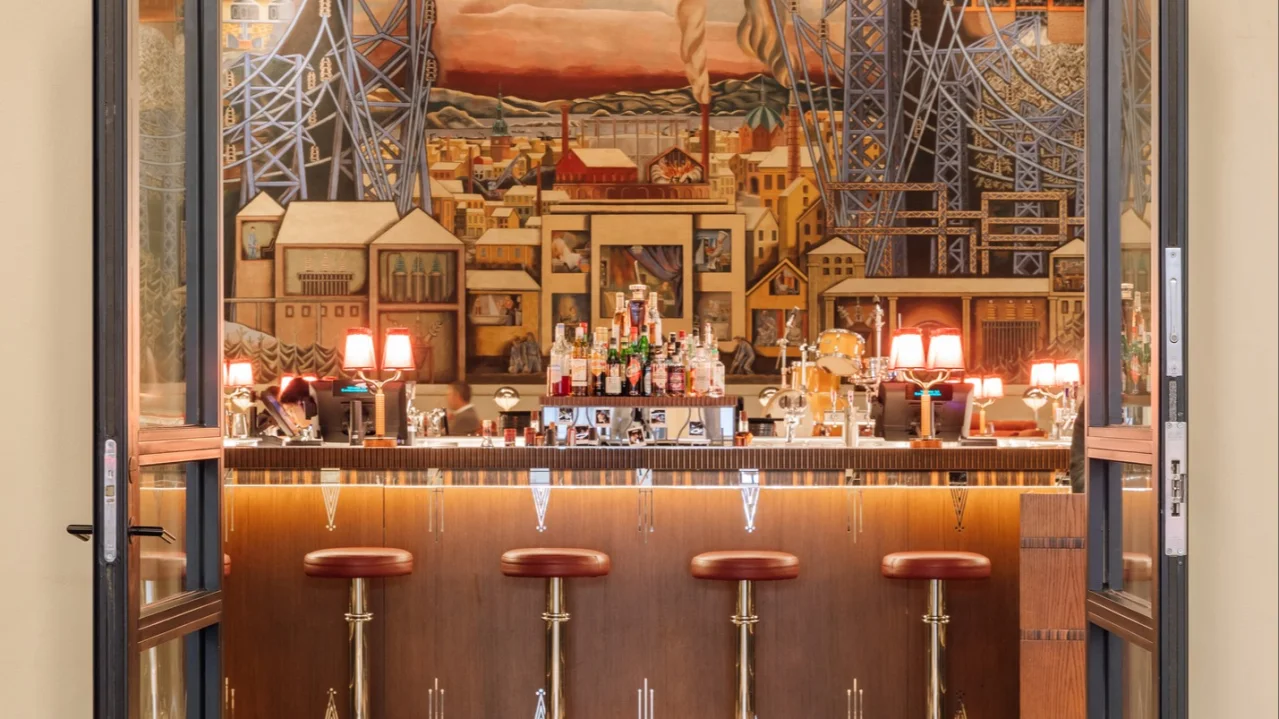 Open doorway revealing a bar with stools and decorative mural; text "EKSPEDISJONS-HALLEN" above door.