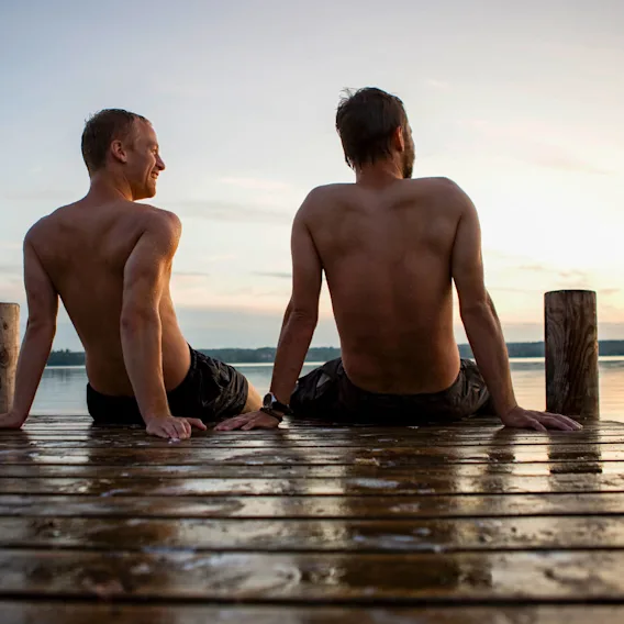 Two guys sitting on the doc after a swim during summer.