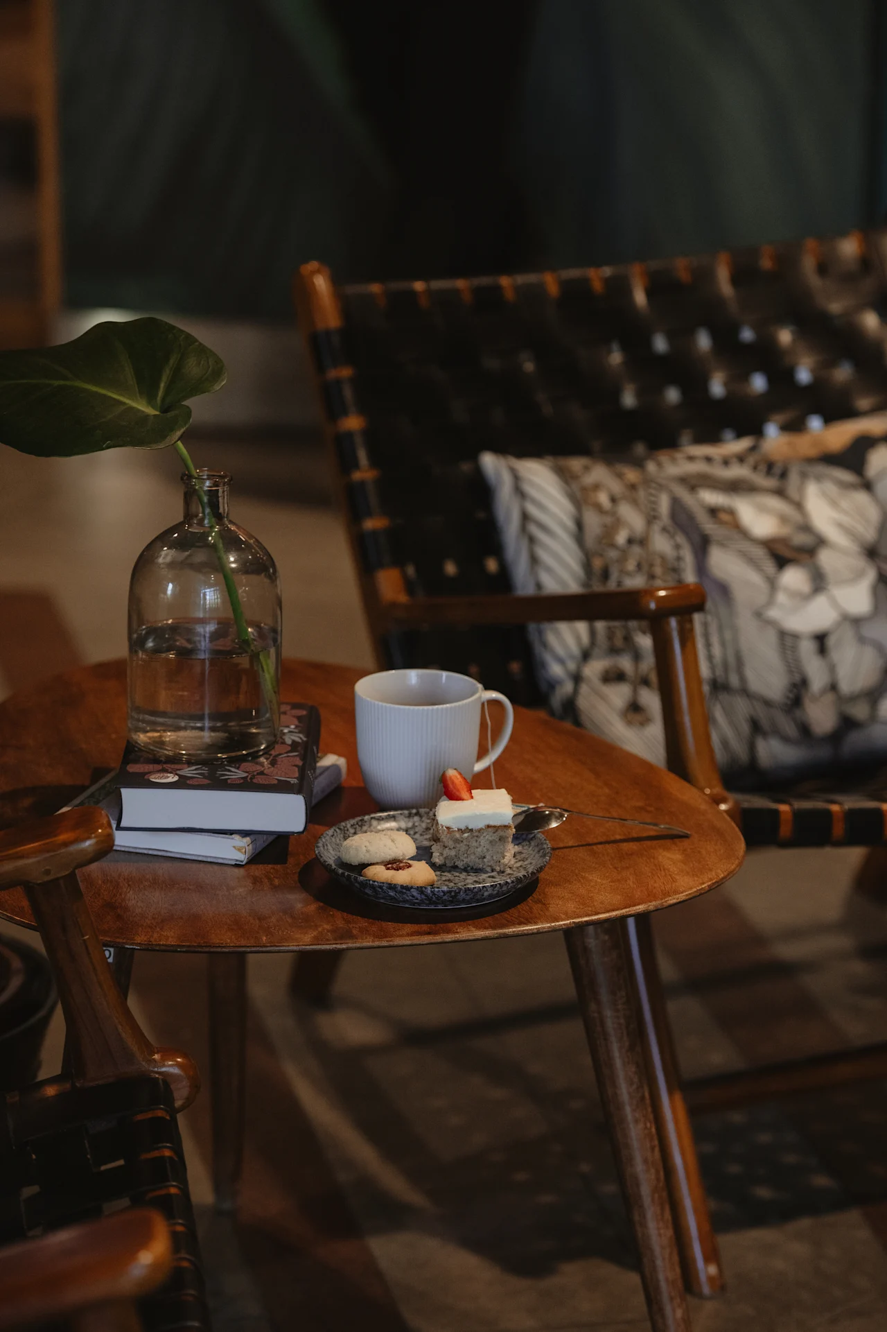 A cozy corner at Home Hotel Uppsala with a wooden table holding books, a cup of tea, and a plate of cake and cookies.
