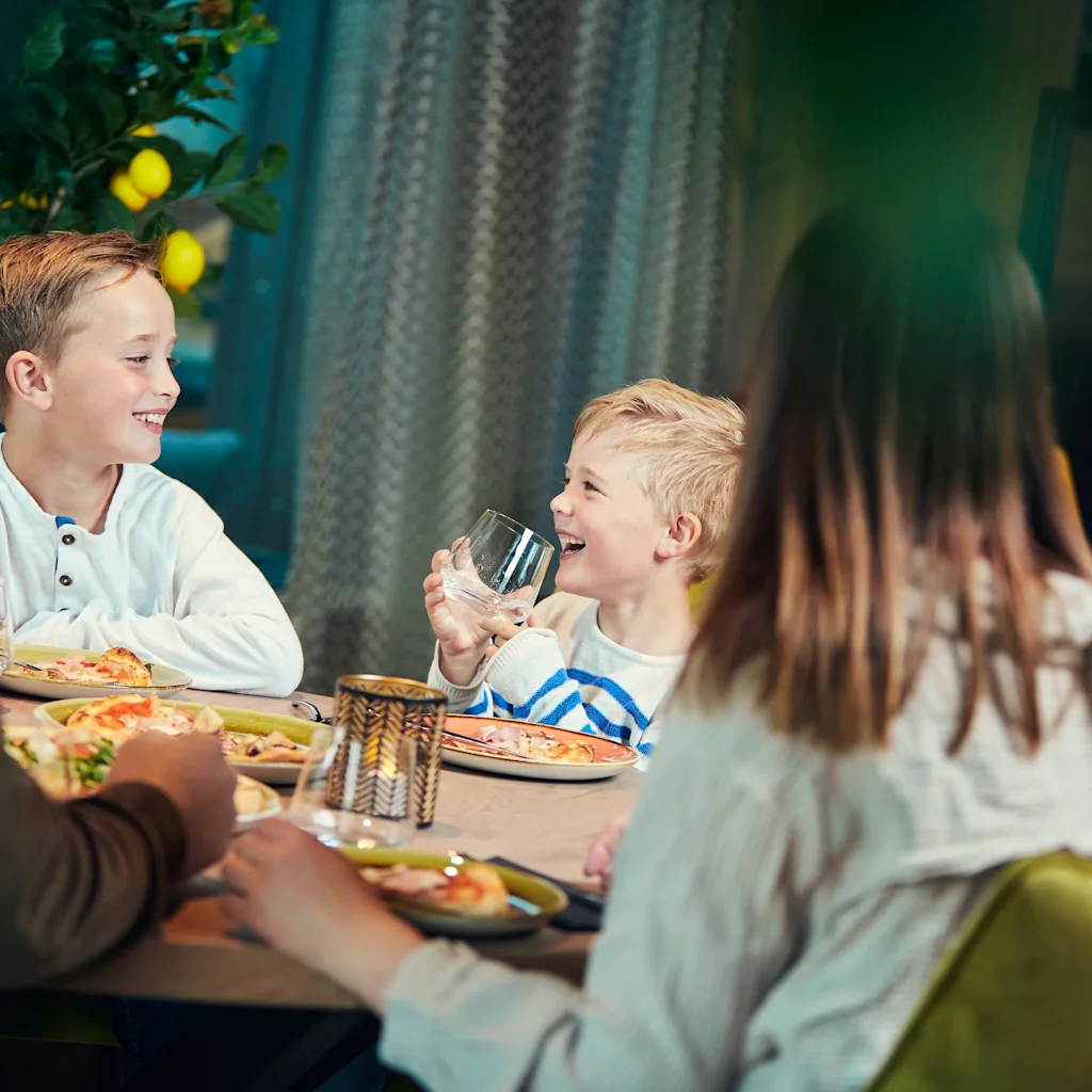 A family enjoying a meal together at a restaurant, with two children smiling and laughing at the table.