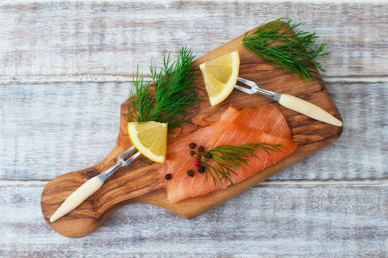 Cured salmon with dill and lemon on a wooden cutting board.