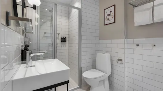 A contemporary bathroom with white tiled walls, a vanity with a sink, a glass shower, and a toilet. A wall art piece displays FLOWERS.
