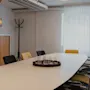 Valoisa kokoushuone, jossa pitkä pöytä, keltaisia ja mustia tuoleja, naulakko ja ikkuna valkoisine verhoineen.