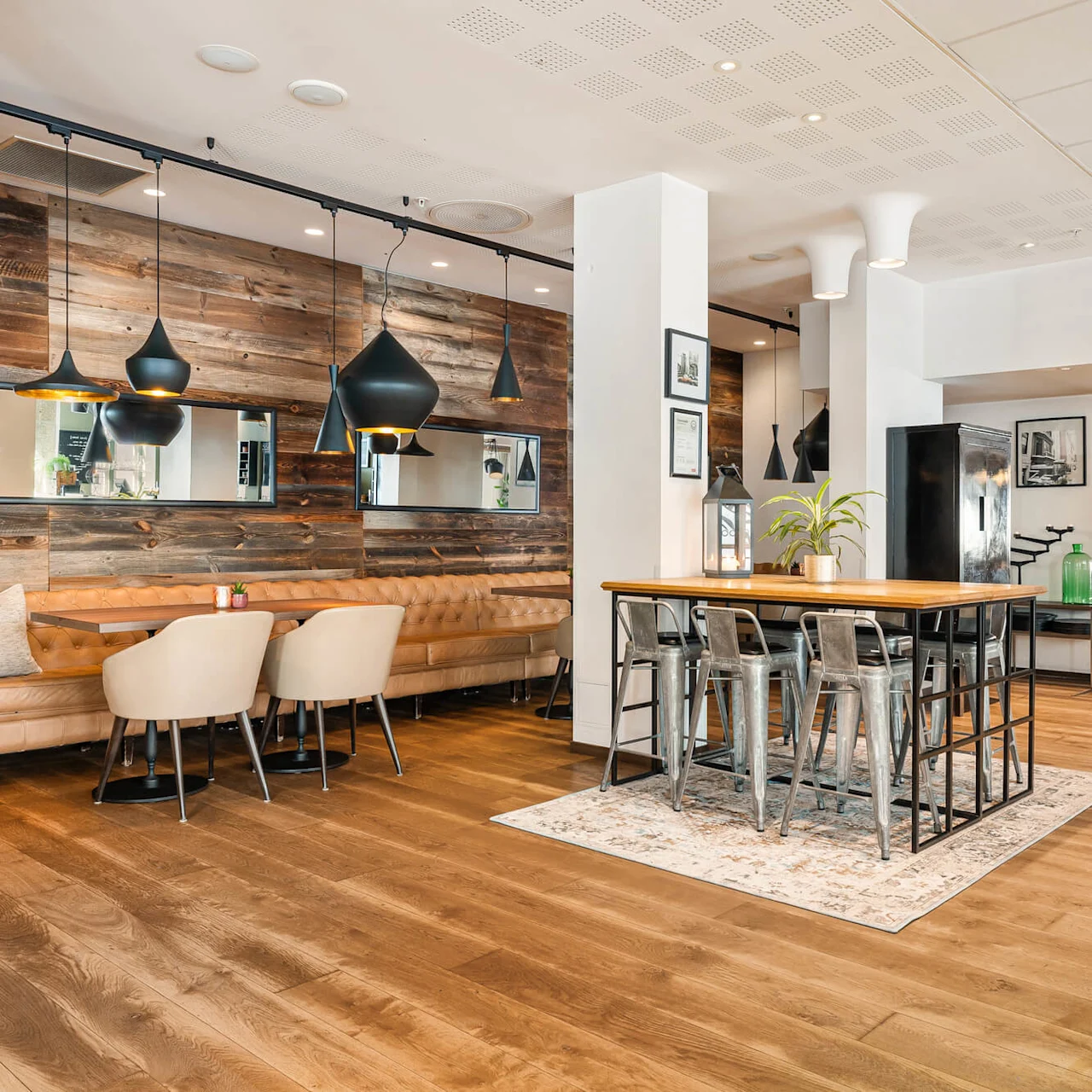 En rummelig restaurantinteriør med trægulv, lædersæder og metalstole omkring træborde. Hængelamper over, og et "RESTAURANT"-skilt er synligt på væggen.