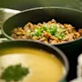 A buffet spread featuring a pot of seasoned chicken with green onions and a pot of creamy soup. Home Hotel Grand Bodø.