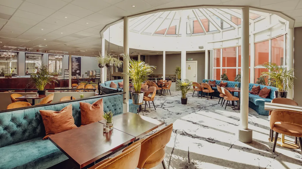 En elegant lounge med bløde siddepladser og potteplanter under et solbelyst atrium.