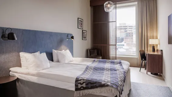 A neatly made bed in a modern hotel room with natural light from a window.