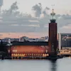 Tukholman kaupungintalo seisoo kauniina veden äärellä rauhallisen auringonlaskun aikaan pilvisellä taivaalla.