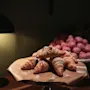 Lähikuva kasasta kullanruskeita croissanteja tomusokerilla, telineellä lampun ja vaaleanpunaisten leivonnaisten kanssa taustalla.