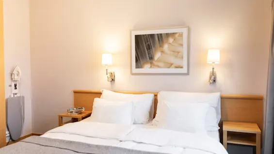 Et koselig hotellrom med en pent oppredd seng, nattbord og varm belysning, som tilbyr et komfortabelt opphold.