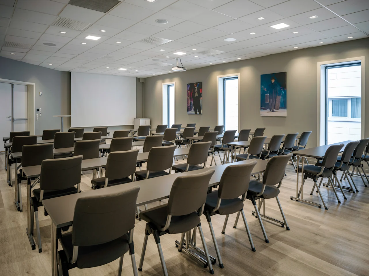 A modern conference room with rows of tables and chairs facing a large projection screen, ready for a presentation or meeting.