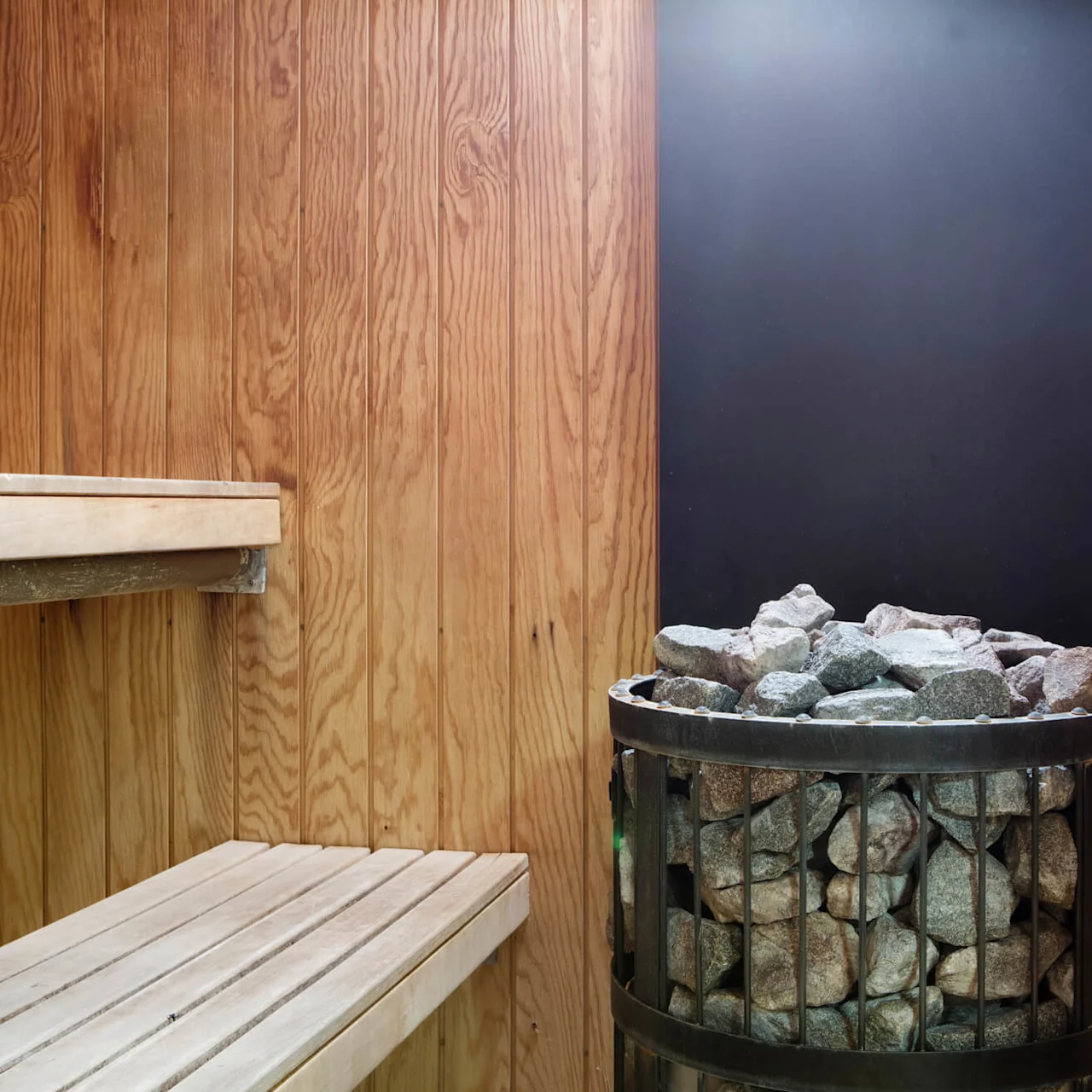 A sauna interior with wooden benches and a heater filled with stones.