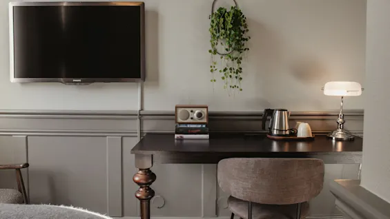 En mysig skrivbordshörna på ett hotellrum med TV, vattenkokare för varma drycker, en lampa och en radio på böcker, vilket skapar en bekväm plats.