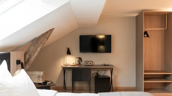 Et moderne hotellrom med skråtak, med en komfortabel seng, et skrivebord med TV og vannkoker, og en garderobe.