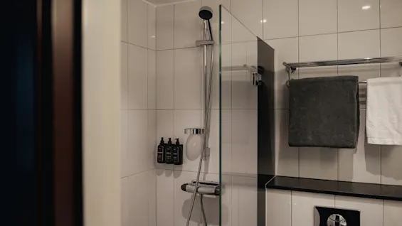 En modern hotellbadrumsdusch med vita kakelplattor, glasskärm, toalettartiklar och fräscha handdukar. Home Hotel Grand, Helsingborg.