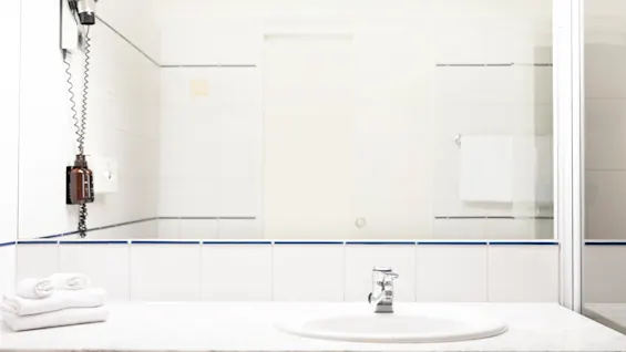 Valoisa kylpyhuoneen pesuallas, hana ja peili. Vastapyyhityt pyyhkeet ja hiustenkuivaaja ovat saatavilla vieraille.