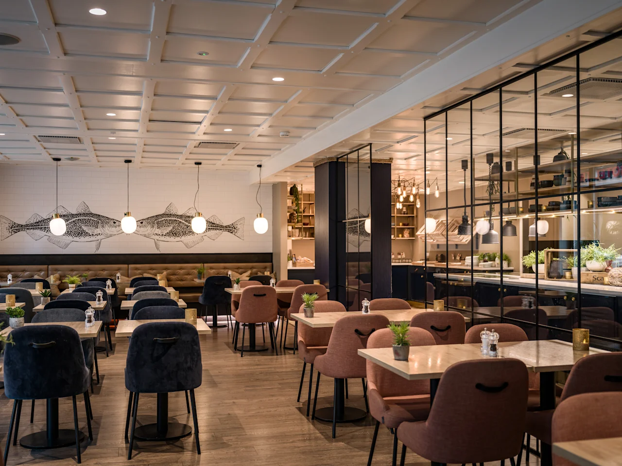 Valoisa ja kutsuva ravintola, jossa on paljon tyhjiä pöytiä ja tuoleja, koristeltu kalataiteella ja tyylikkäällä lasipaneelialueella.