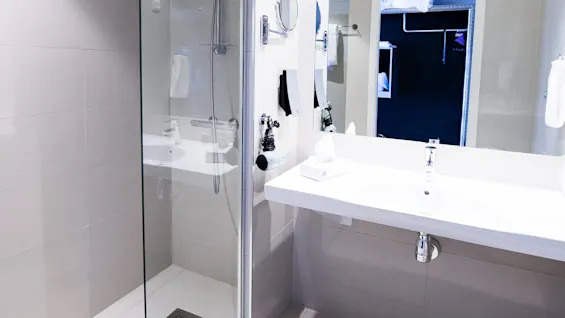 A modern bathroom with glass-walled shower, sink, and mirror, illuminated and clean.