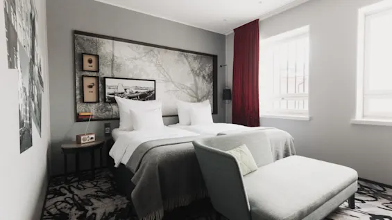 Et moderne hotelværelse med to senge, en chaiselong og en naturinspireret sengegavl.