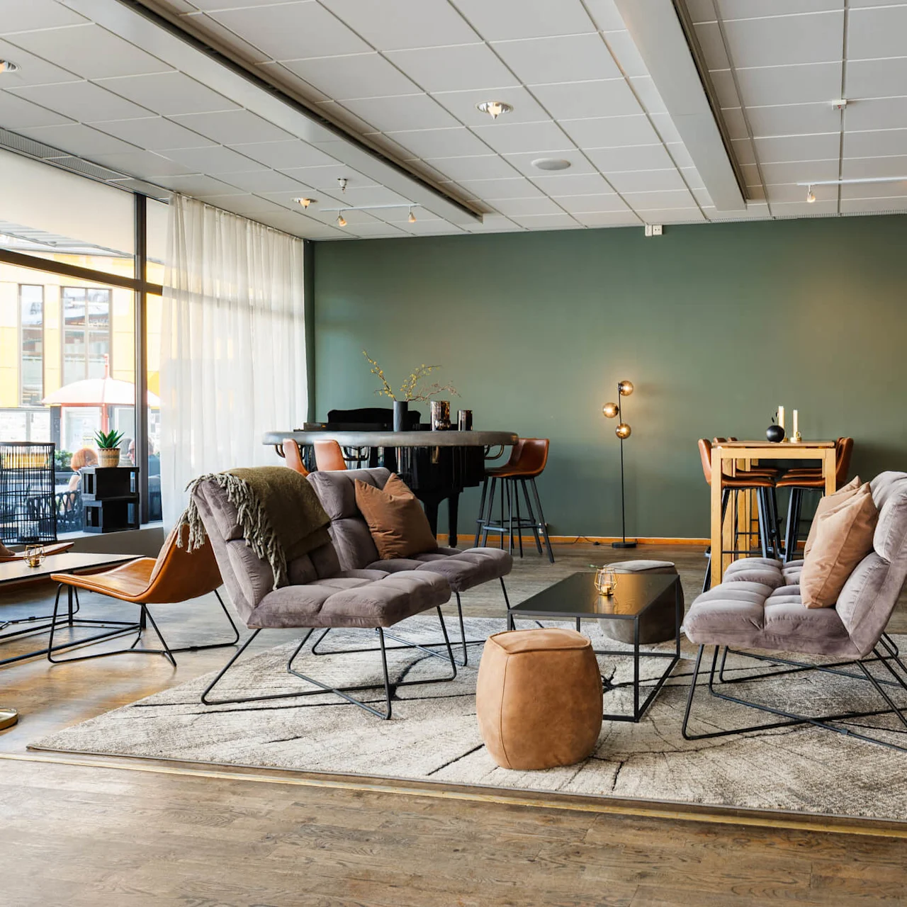 Mysiga loungestolar står på en matta nära ett litet bord, i en varmt upplyst, modern bar. "BAR" visas tydligt på disken, omgiven av dryckeshyllor.