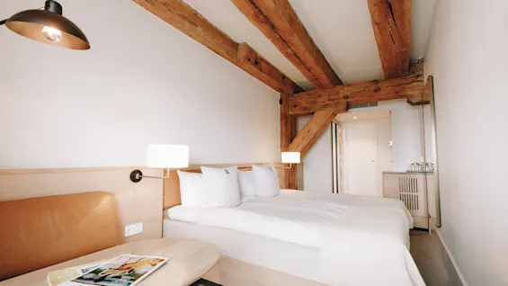 Ett mysigt hotellrum med en bekväm säng, en liten sittgrupp och synliga träbjälkar i taket.